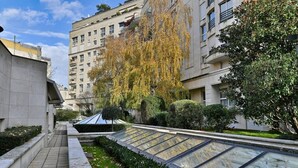 Un edificio residencial de diseño moderno, con un invernadero de vidrio, setos cuidados y árboles maduros.