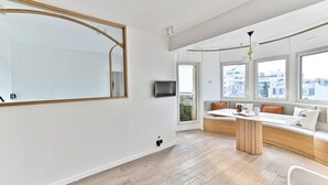 Una sala de estar moderna con un espejo grande, un banco empotrado, un televisor y ventanas amplias.