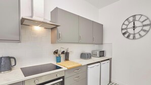 A modern kitchen with grey cabinets, a stainless steel range hood, a microwave, a toaster, and a sink with a cutting board. - Painters Apartment - modern decor, 4 bedrooms, central location. 5 minutes walk to South Bay beach. Fully equipped kitchen. Longer stays welcome. (North Yorkshire)