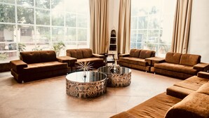 A spacious living room with large windows, brown sofas, and two round coffee tables with floral designs. - BR Resort & Club (Sonkach)