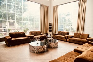 Uma sala de estar espaçosa com grandes janelas, sofás marrons e duas mesas de centro redondas com estampas florais.