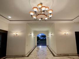Um corredor com lustre, arandelas e piso de mármore.