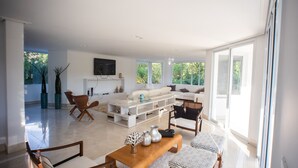 Ein modernes Wohnzimmer mit einer Couch, Sesseln, einem Couchtisch und einem an der Wand befestigten Fernseher.