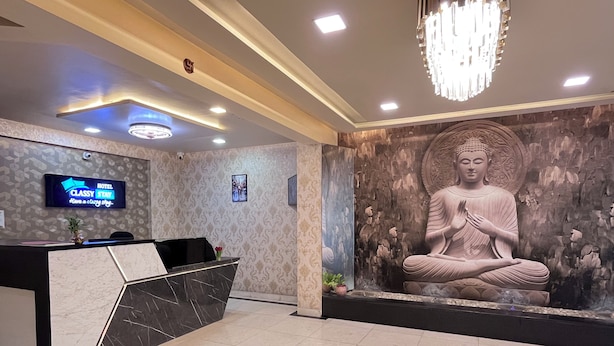 Et hotelreceptionsområde med et moderne design, inklusive en receptionsdisk, en Buddha-statue og et digitalt skærm, der viser hotellets navn.