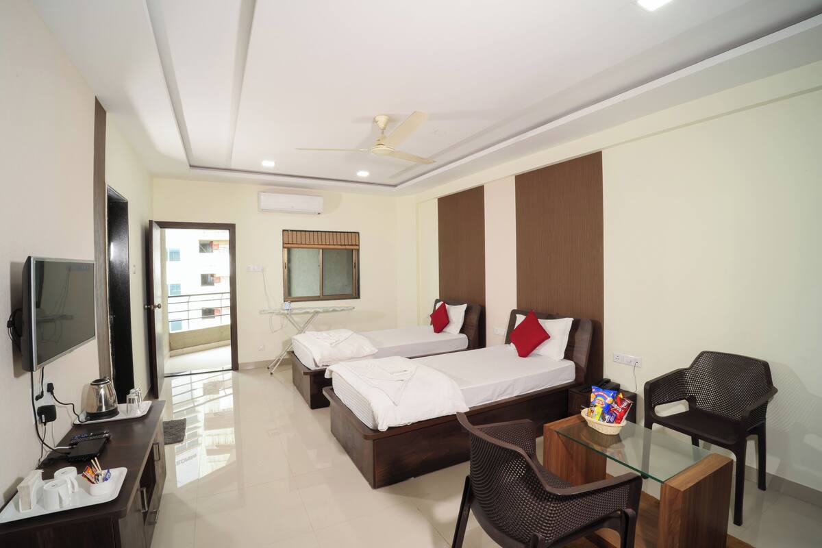 A hotel room with two beds, a desk with a chair, a TV, and a balcony view.