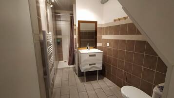 Ein schmales Badezimmer mit Dusche, Waschbecken und Toilette.