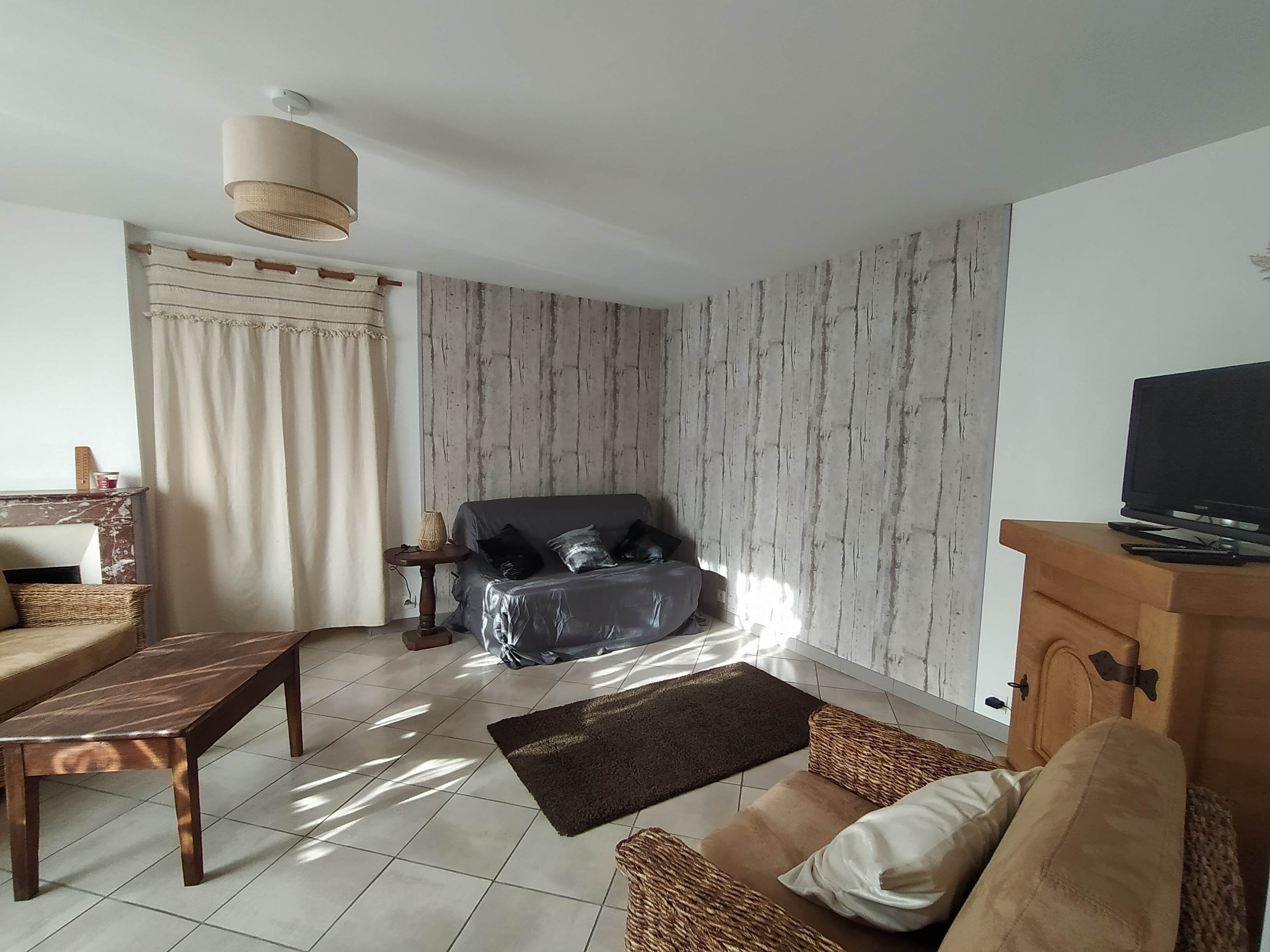 A living room with a sofa, a wooden coffee table, a television on a wooden cabinet, and a patterned wall.