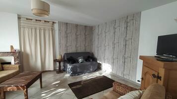 A living room with a sofa, a wooden coffee table, a television on a wooden cabinet, and a patterned wall.