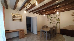 Ein gemütliches Zimmer mit einem Holztisch, einem Esstisch mit Stühlen und einer Decke mit sichtbaren Balken und Lichterkette.