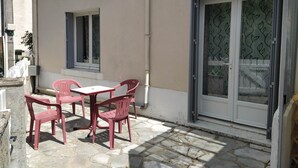 Ein Gebäude mit einer gepflasterten Terrasse, einem Tisch mit Stühlen und einer Glastür mit Blattmuster.