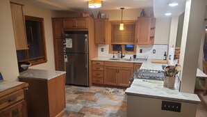 A kitchen with wooden cabinets, a stainless steel refrigerator, a gas stove, and a tiled floor. - Multi-week rental directly on Chandler Lake  deck, fire pit, tandem kayak. (Traverse City)