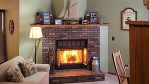 A cozy living room with a brick fireplace, a sofa, and a chair. - Multi-week rental directly on Chandler Lake  deck, fire pit, tandem kayak. (Traverse City)