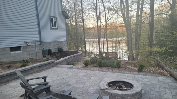 A patio area with Adirondack chairs, a fire pit, and a view of a lake surrounded by trees. - Multi-week rental directly on Chandler Lake  deck, fire pit, tandem kayak. (Traverse City)