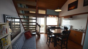 A cozy kitchen with a dining area, wooden staircase, and a large window.
