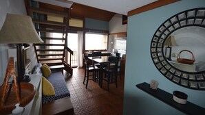 A dining area with a wooden table and chairs, a large mirror on the wall, and a view of the kitchen through an open door.