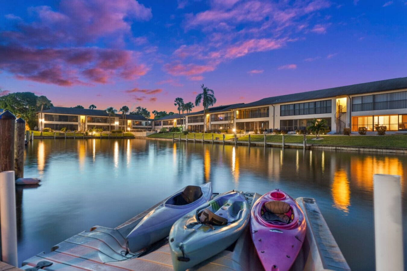 A waterfront hotel with kayaks docked at the pier, reflecting the building and sky.