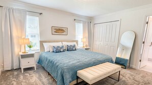 A bedroom with a bed, bedside tables, a bench, a mirror, and a door. - Storey Lake 4BR Townhome w/ Private Pool (Kissimmee)