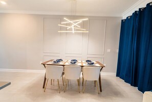 A dining area with a modern chandelier, a table set for four, and a blue curtain. - Storey Lake 4BR Townhome w/ Private Pool (Kissimmee)