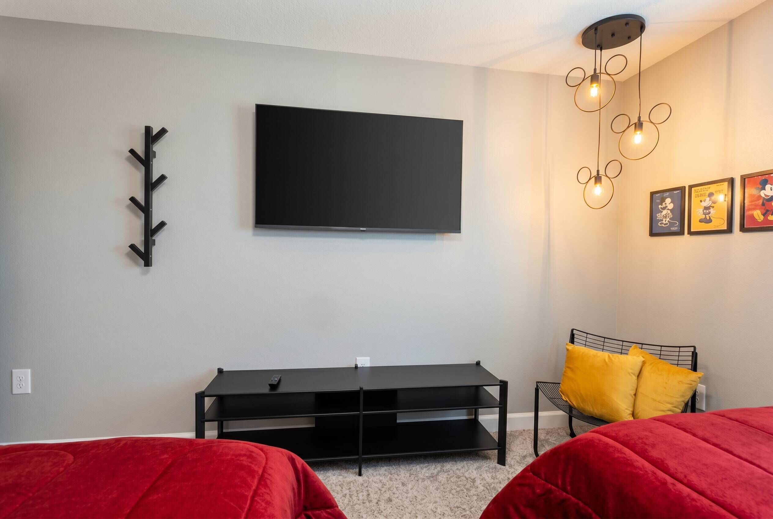 A bedroom with a TV, a black TV stand, a bed with red bedding, a yellow pillow, and a Mickey Mouse light fixture.