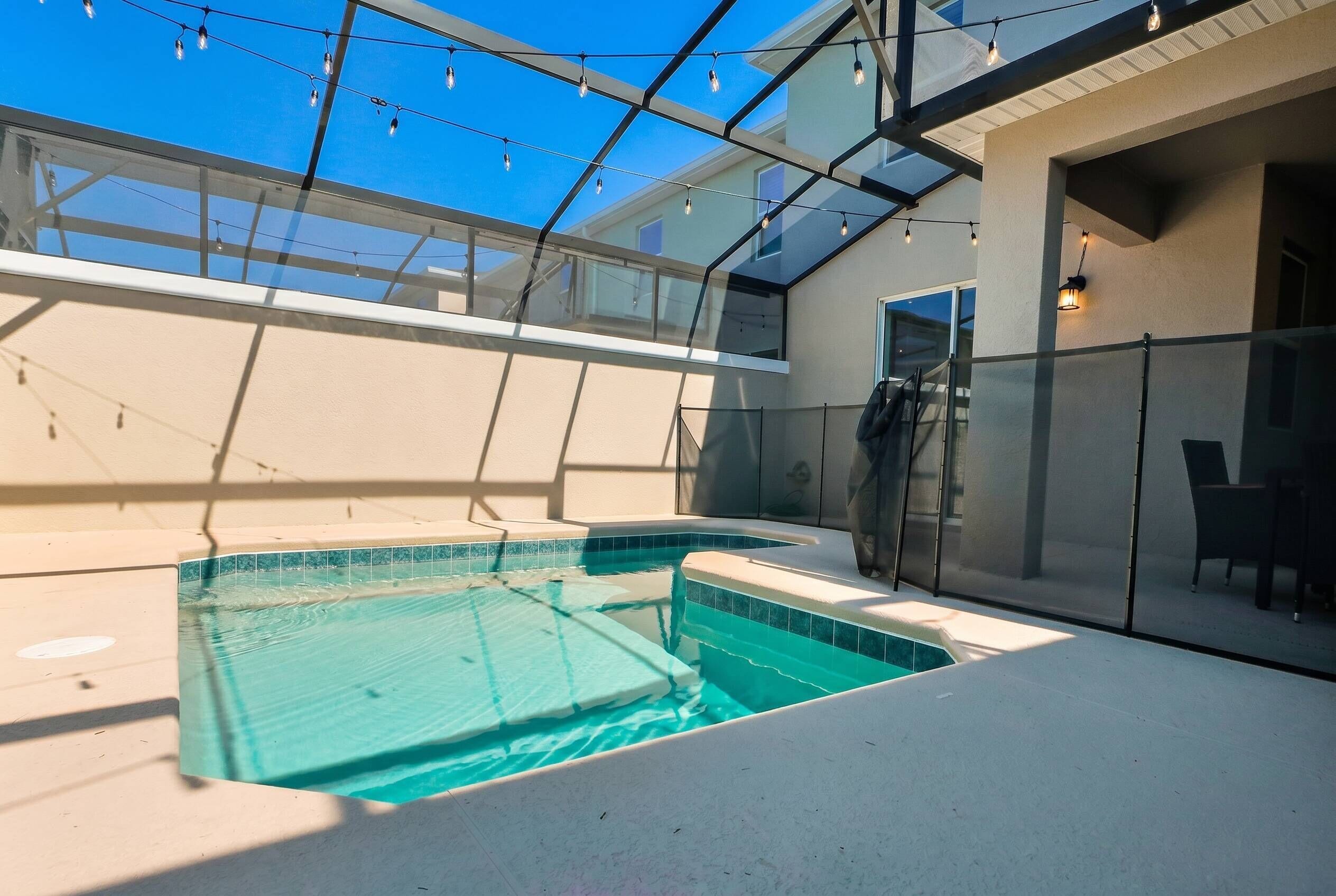Ein Schwimmbad mit Glasumrandung, Lichterketten und einer überdachten Terrasse.