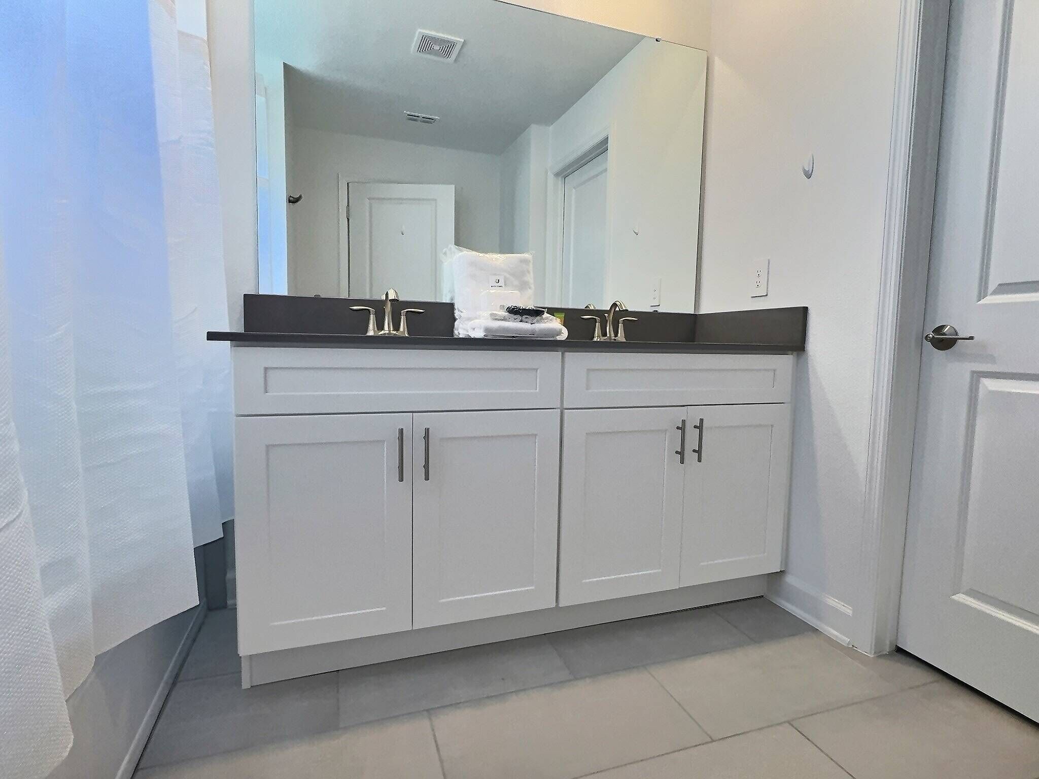 A bathroom with a double sink vanity, white cabinets, and a large mirror.