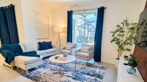 A living room with a sofa, armchairs, a coffee table, a lamp, and a large window with curtains. - Storey Lake 4BR Townhome w/ Private Pool (Kissimmee)
