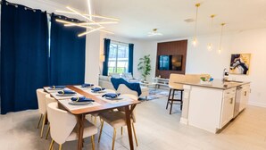 A modern dining area with a wooden table, white chairs, and blue napkins. - Storey Lake 4BR Townhome w/ Private Pool (Kissimmee)