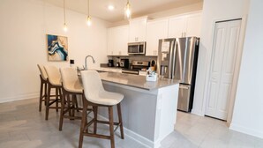 A modern kitchen with white cabinets, stainless steel appliances, and a central island with bar stools. - Storey Lake 4BR Townhome w/ Private Pool (Kissimmee)