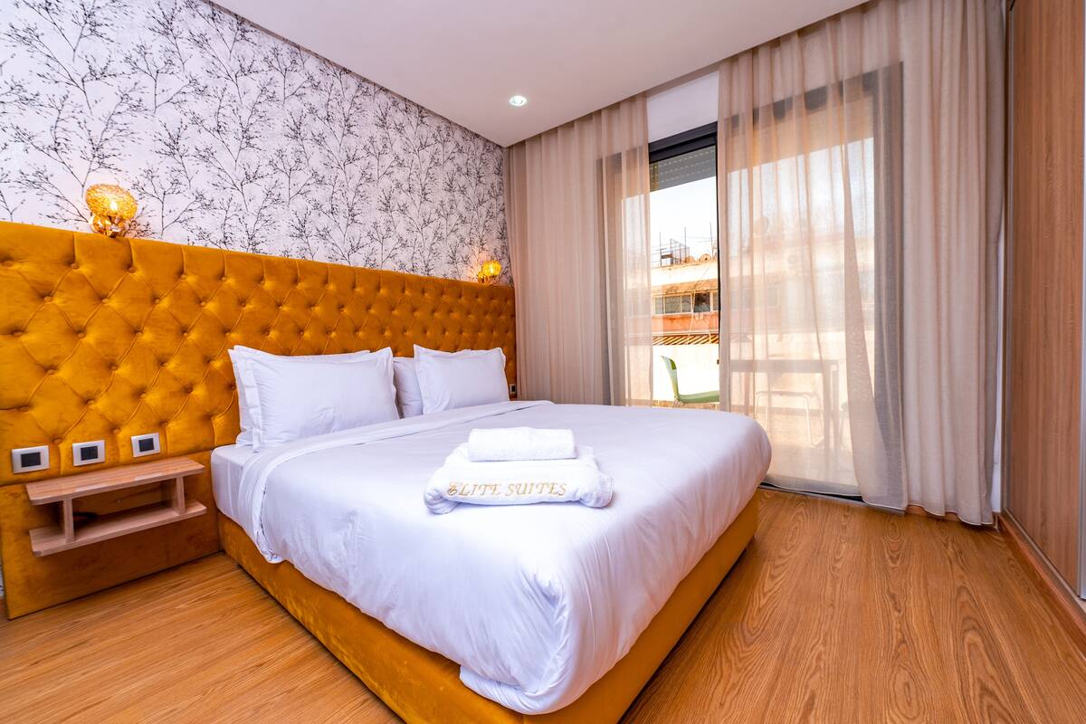 Hotelkamer met een groot bed, een houten hoofdeinde, een nachtkastje en een raam met gordijnen.