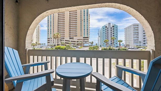 A balcony with blue chairs and a table, overlooking a parking area and high-rise buildings. - Sun, sand & serenity ~ The Good Life! (Gulf Shores)