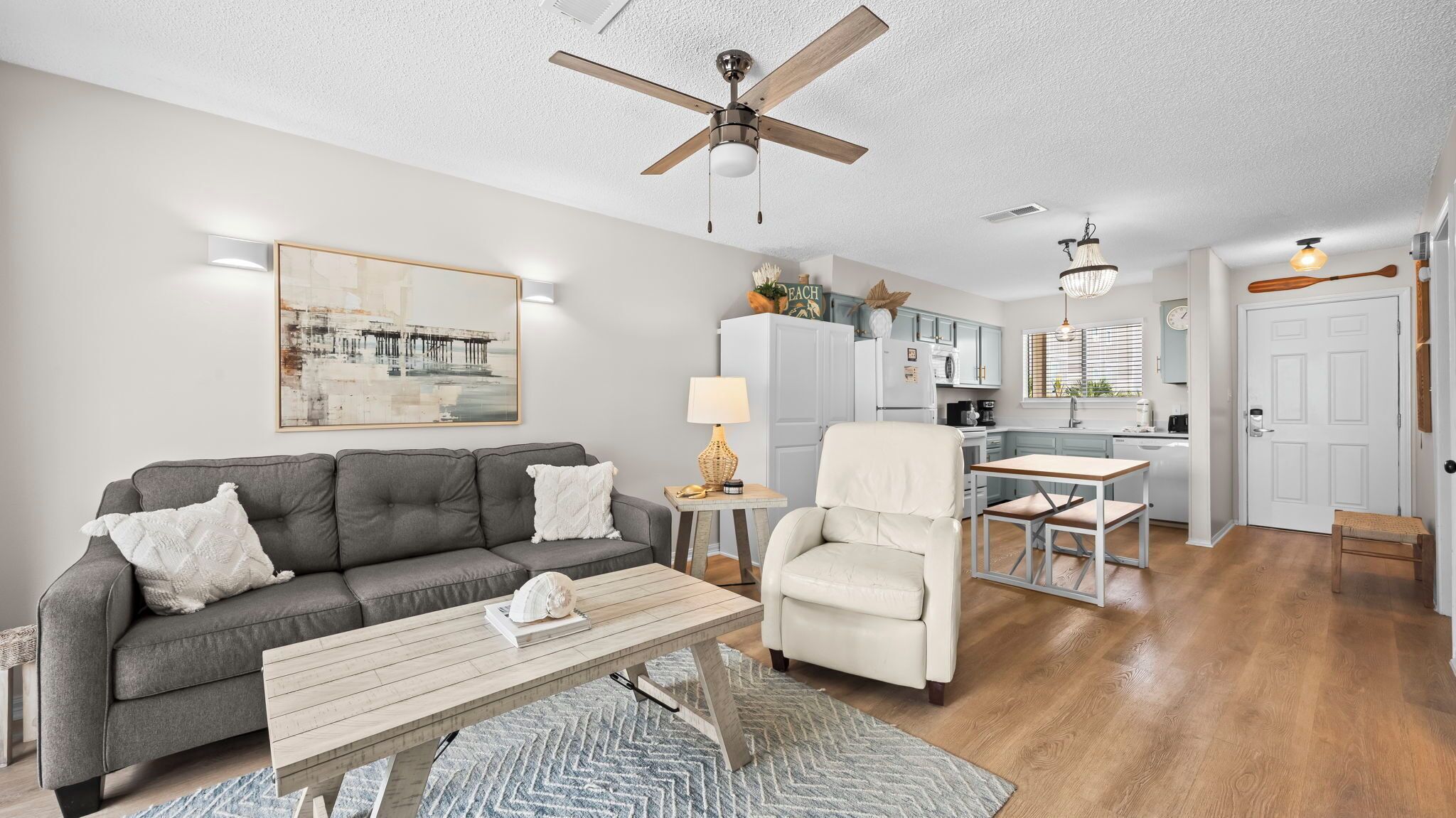 A living room with a grey sofa, a white armchair, a wooden coffee table, and a dining area with a small table and chairs.