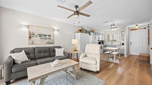 A living room with a grey sofa, a white armchair, a wooden coffee table, and a dining area with a small table and chairs. - Sun, sand & serenity ~ The Good Life! (Gulf Shores)