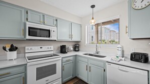 A kitchen with white appliances, light blue cabinets, a window with blinds, and a clock on the wall. - Sun, sand & serenity ~ The Good Life! (Gulf Shores)