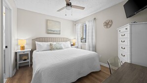 A bedroom with a bed, bedside tables, a dresser, a ceiling fan, a painting, and a window with curtains. - Sun, sand & serenity ~ The Good Life! (Gulf Shores)