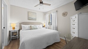 A bedroom with a bed, bedside tables, a dresser, a ceiling fan, a painting, and a window with curtains. - Sun, sand & serenity ~ The Good Life! (Gulf Shores)