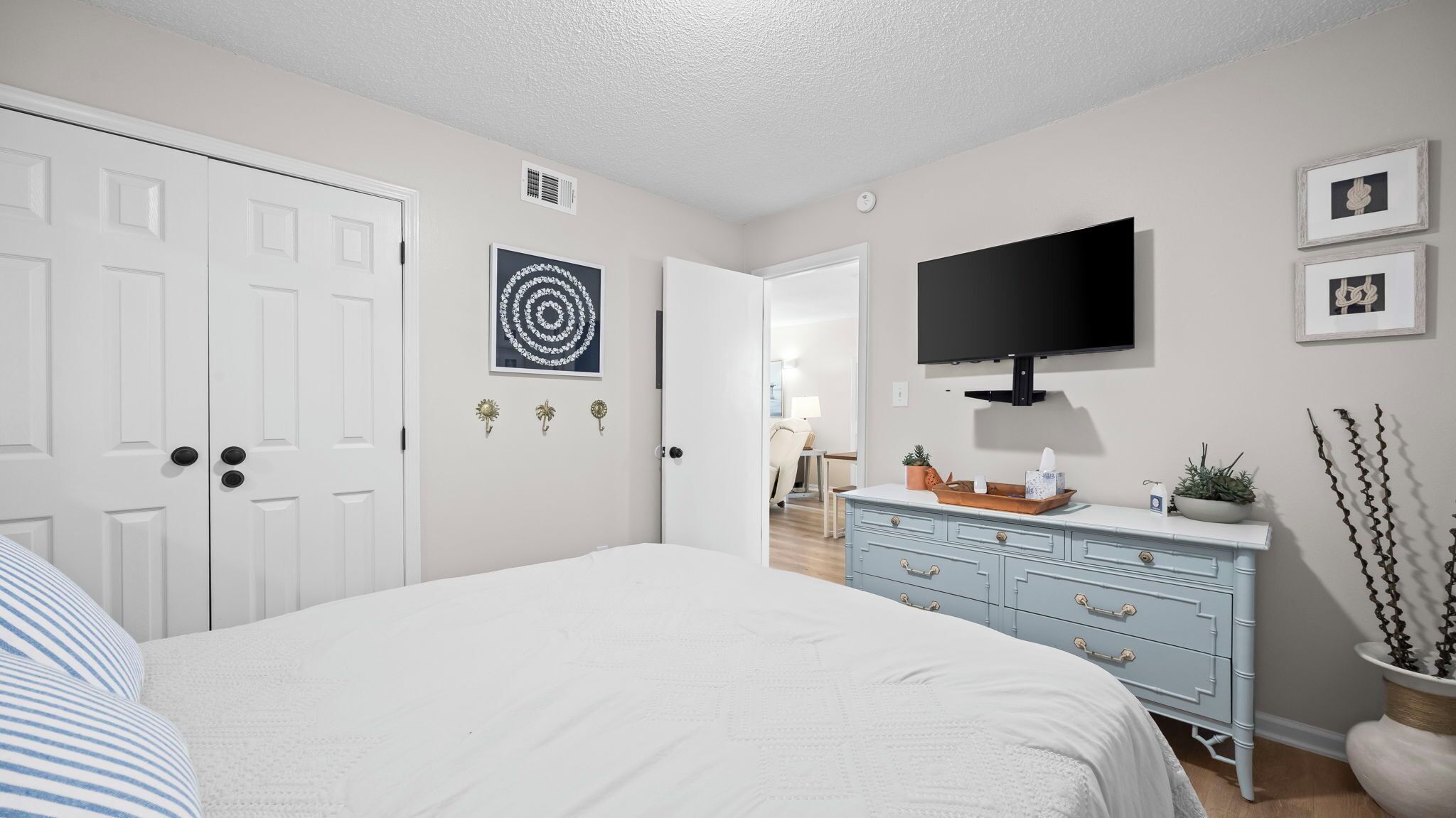 A bedroom with a bed, dresser, TV, and artwork.