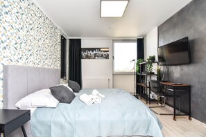 Una camera da letto moderna con un letto, una scrivania, una TV e vista sulla città.