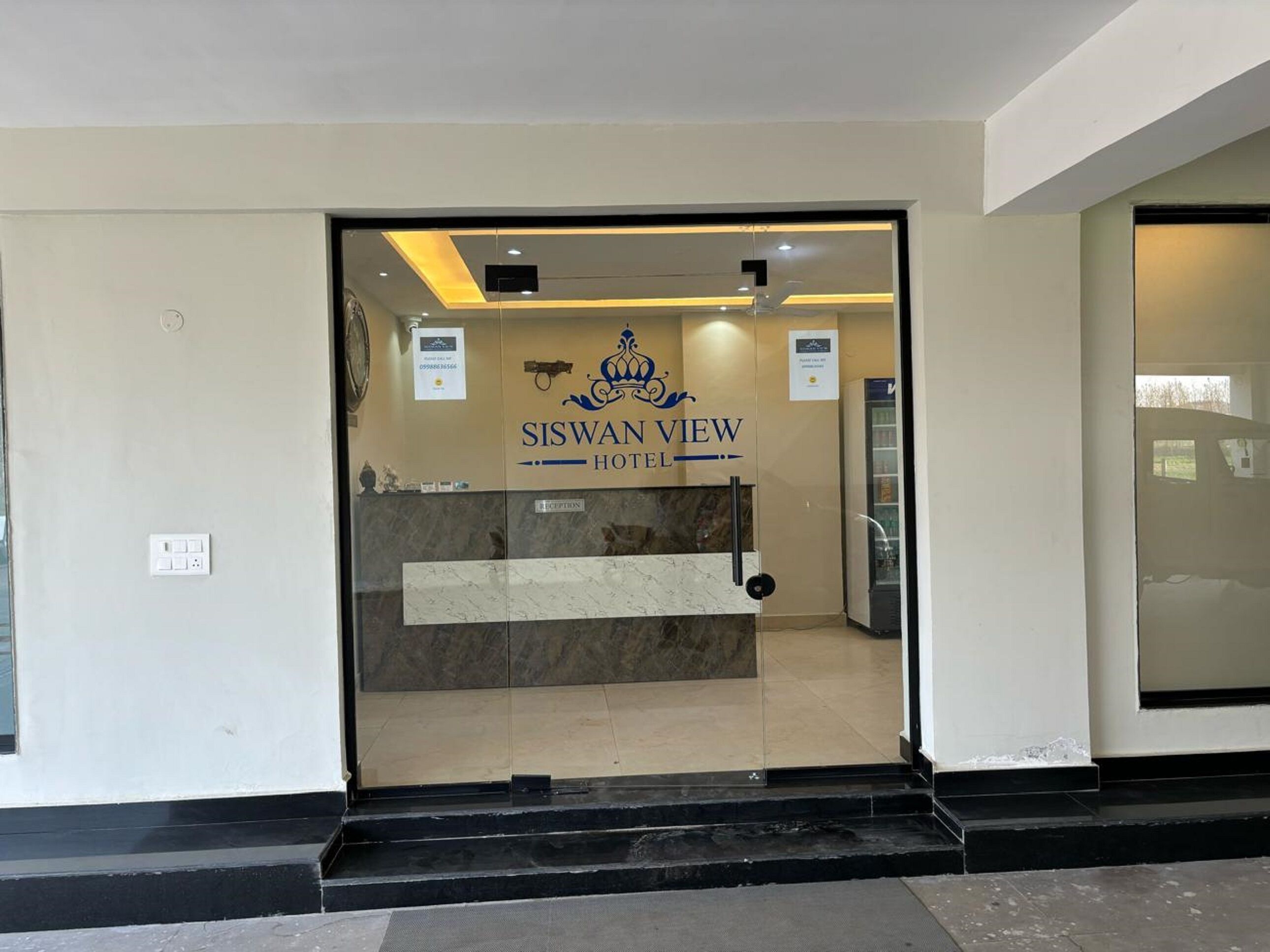 The entrance to the Siswan View Hotel with a reception desk and a glass door.