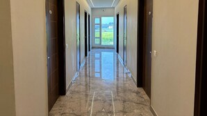 A hallway with a marble floor, wooden doors, and a view of greenery outside. - Siswan View Hotel (Kharar)