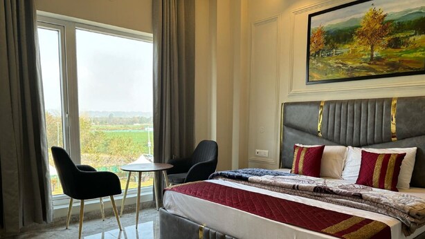 A bedroom with a large bed, a small table, two chairs, and a painting on the wall. - Siswan View Hotel (Kharar)