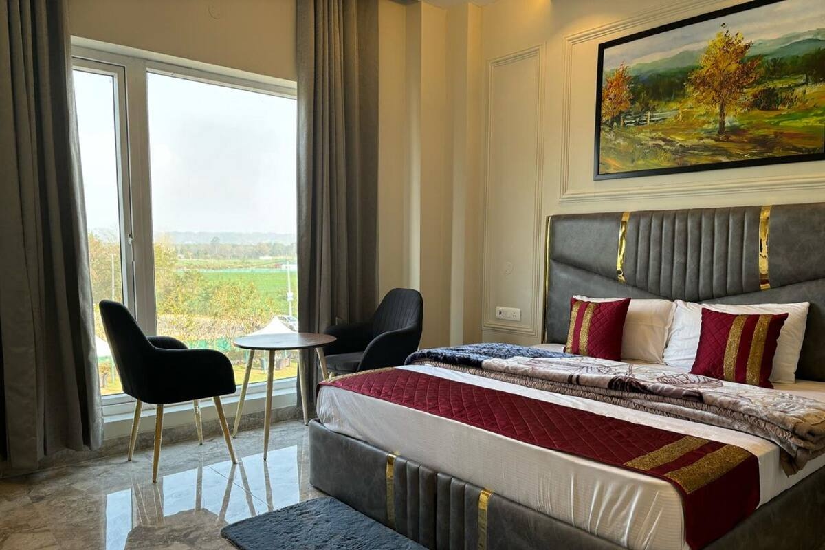 A bedroom with a large bed, a small table, two chairs, and a painting on the wall.