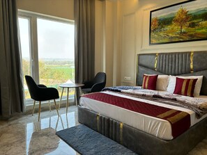 Une chambre à coucher avec un grand lit, une petite table, deux chaises et un tableau accroché au mur.