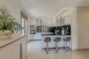 Una cocina moderna con una isla central, taburetes de bar y una planta en maceta.