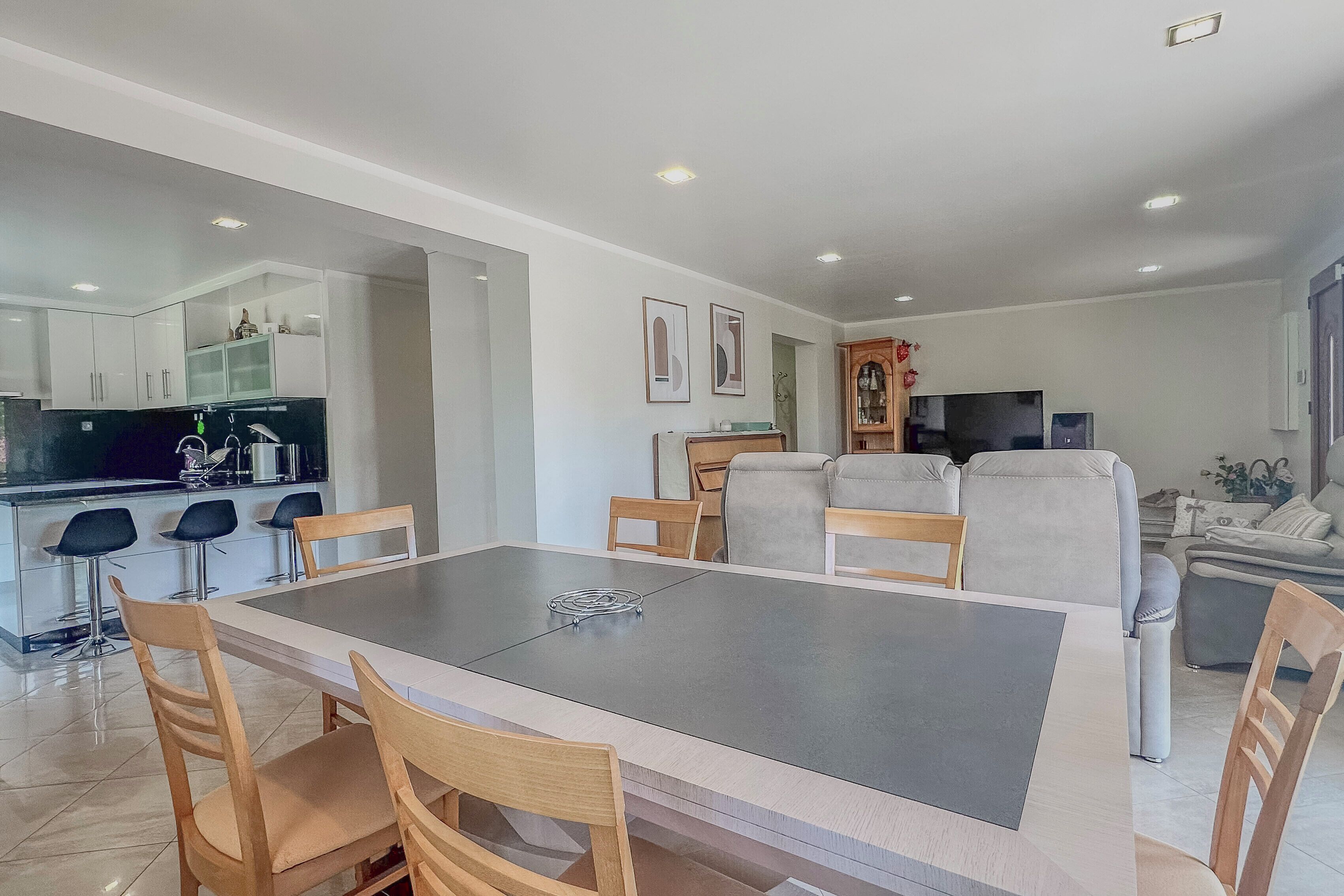 Une cuisine moderne avec des meubles blancs, une table à manger avec des chaises et un coin salon avec un canapé et un téléviseur.