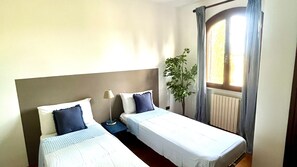 A twin room with two single beds, a bedside table with a lamp, a potted plant, and a window with curtains. - Tuscan Villa 5mins From Beach, Sleeps 8, ev Point (Campiglia Marittima)