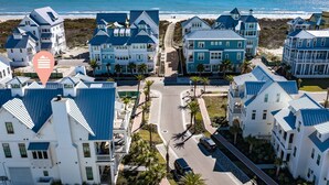 A coastal residential area with multiple two-story houses featuring blue and white exteriors, a beach in the background, and a clear sky.