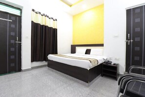 A hotel room with a single bed, a bedside table with a phone, and a chair. - Hotel Vedic Inn (Kiraoli)