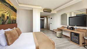 Una camera d'albergo con un letto, una scrivania, una televisione e un'ampia finestra vista vigneti.