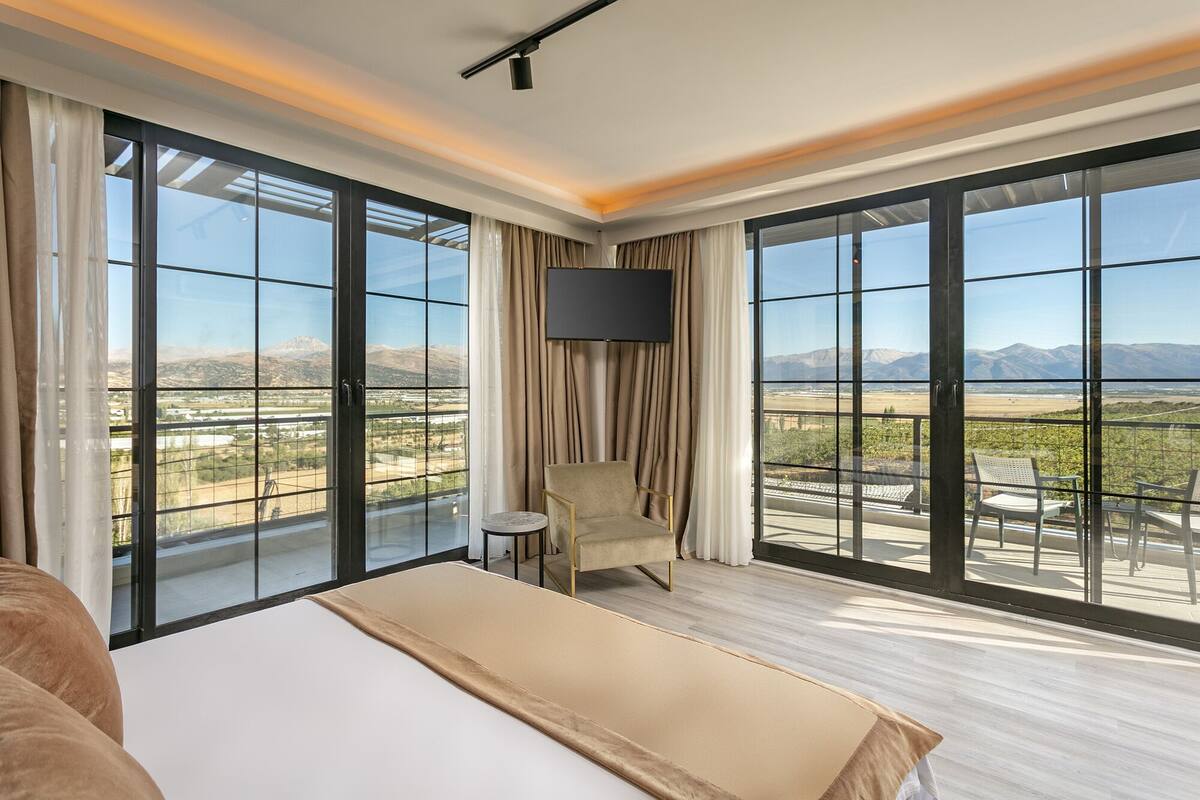 A hotel room with a large bed, a TV, and a balcony with a mountain view.