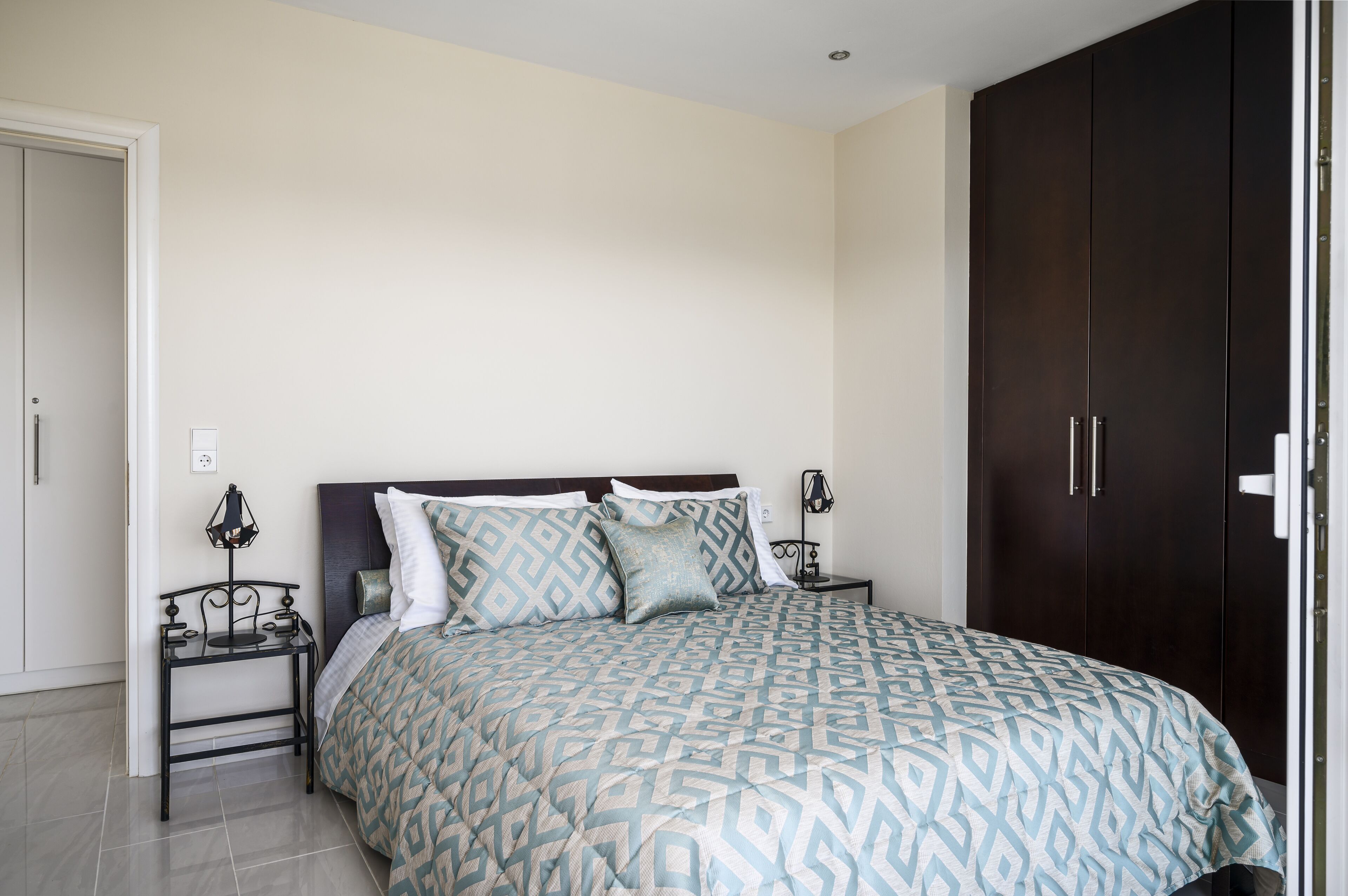 A bedroom with a bed, a nightstand, a wardrobe, and a door.